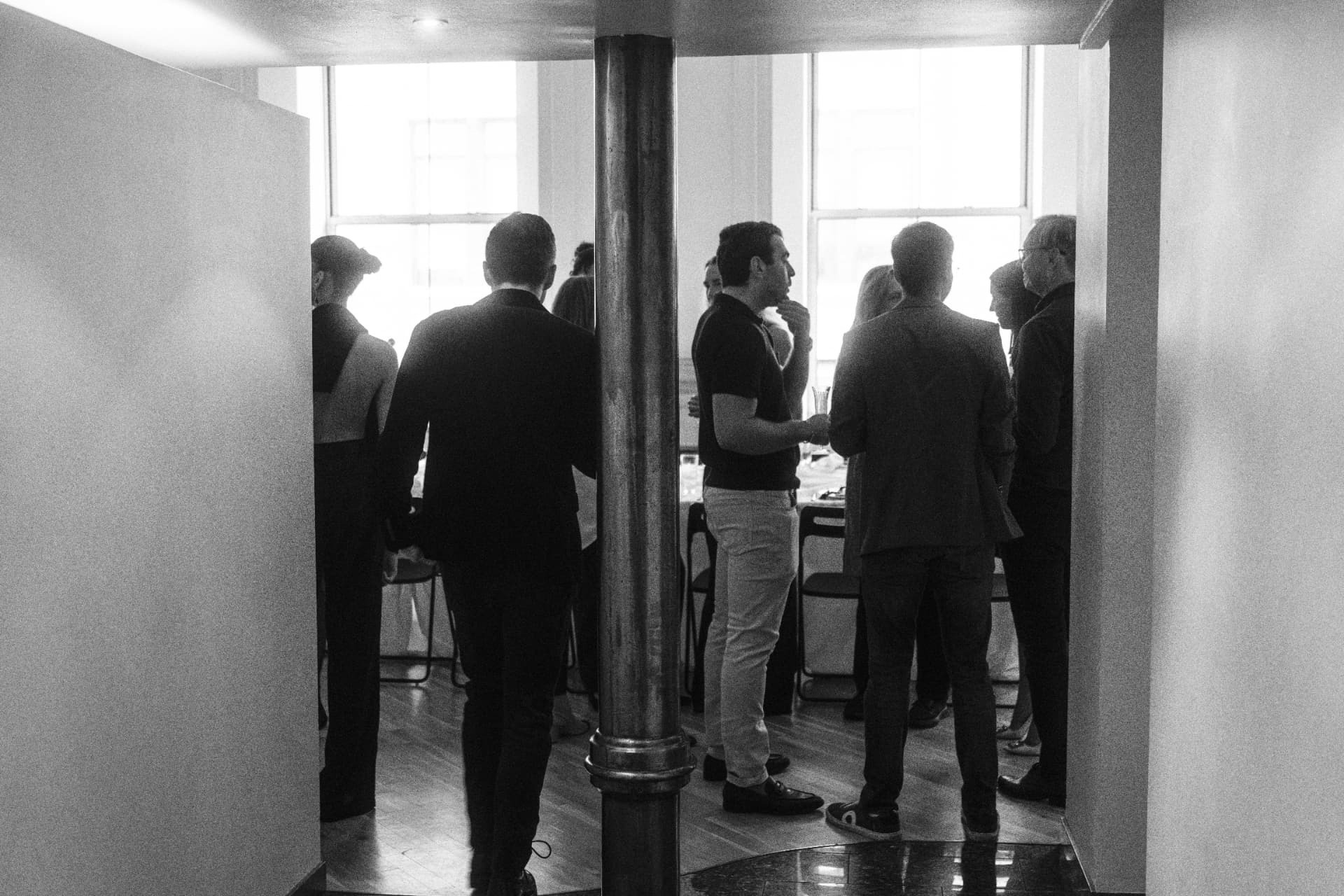 Guests standing in conversation near a window, backlit into near-silhouette