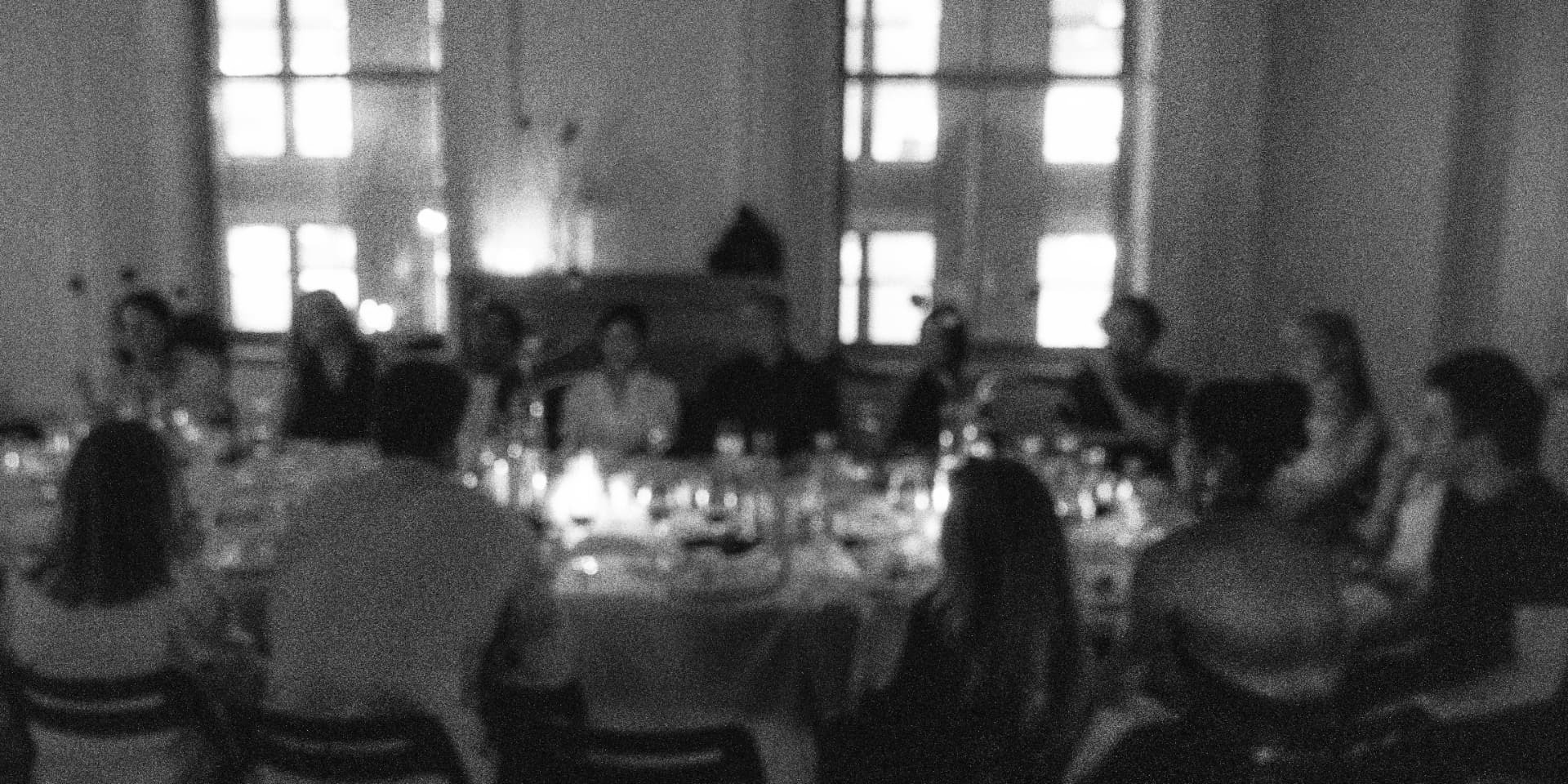 Motion-blurred black-and-white photograph of candlelight at a Cureators table